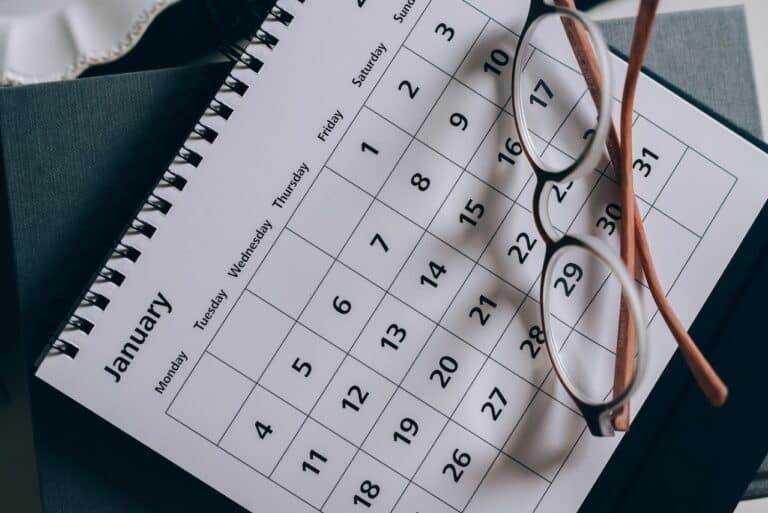 A spiral-bound January calendar rests on a dark surface, subtly marking the beginning of an Oregon divorce timeline. Brown-framed eyeglasses are placed diagonally over the top right corner, adding a casual touch to the scene.